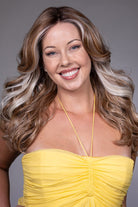 Smiling woman wearing a long, wavy blonde wig with light blonde money piece highlights and a wide center part.