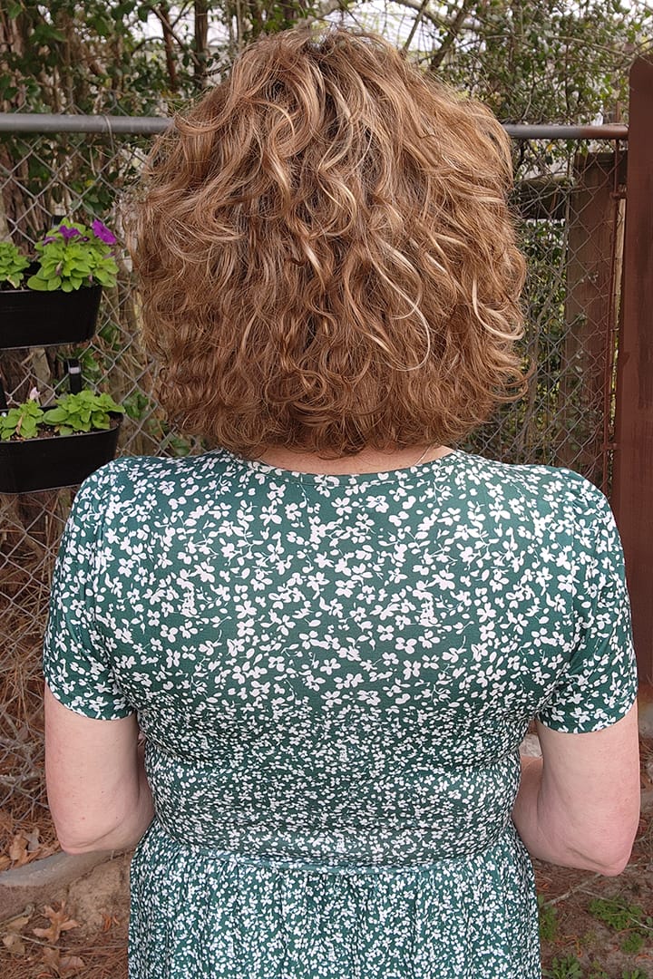 Woman wearing curly bob wig (Loop by Ellen Wille in color Tobacco R) back