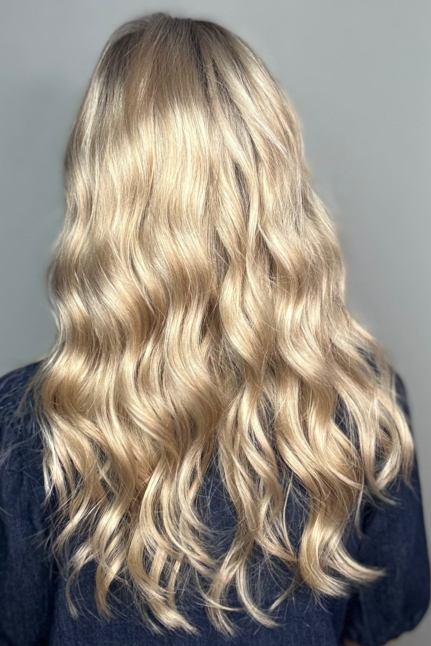 Woman with long rooted blonde wavy wig. (Maya Hand-Tied by Envy in Silky Beige).