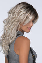 Woman wearing Verona Synthetic Wig in color Vanilla Macchiato by Estetica with a white background and grey tank top - Side / back view.