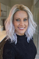 A smiling woman with shoulder-length wavy pink wig (Somers by Estetica in Polarizing Pink).