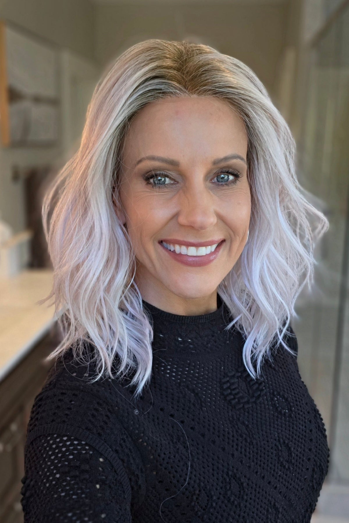 A smiling woman with shoulder-length wavy pink wig (Somers by Estetica in Polarizing Pink).