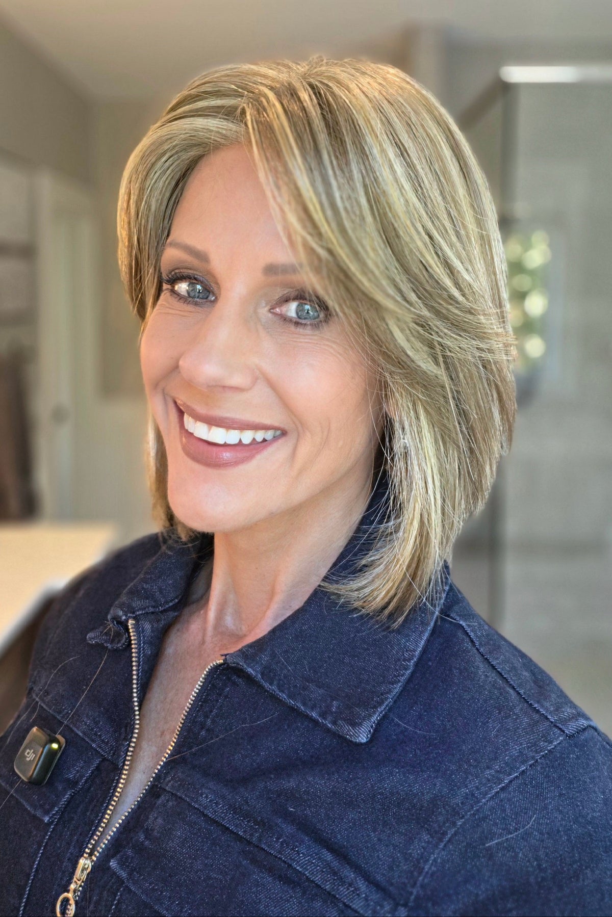 A smiling woman wearing a blonde bob wig with side bangs (Lark by Estetica in color R12/26CH). 