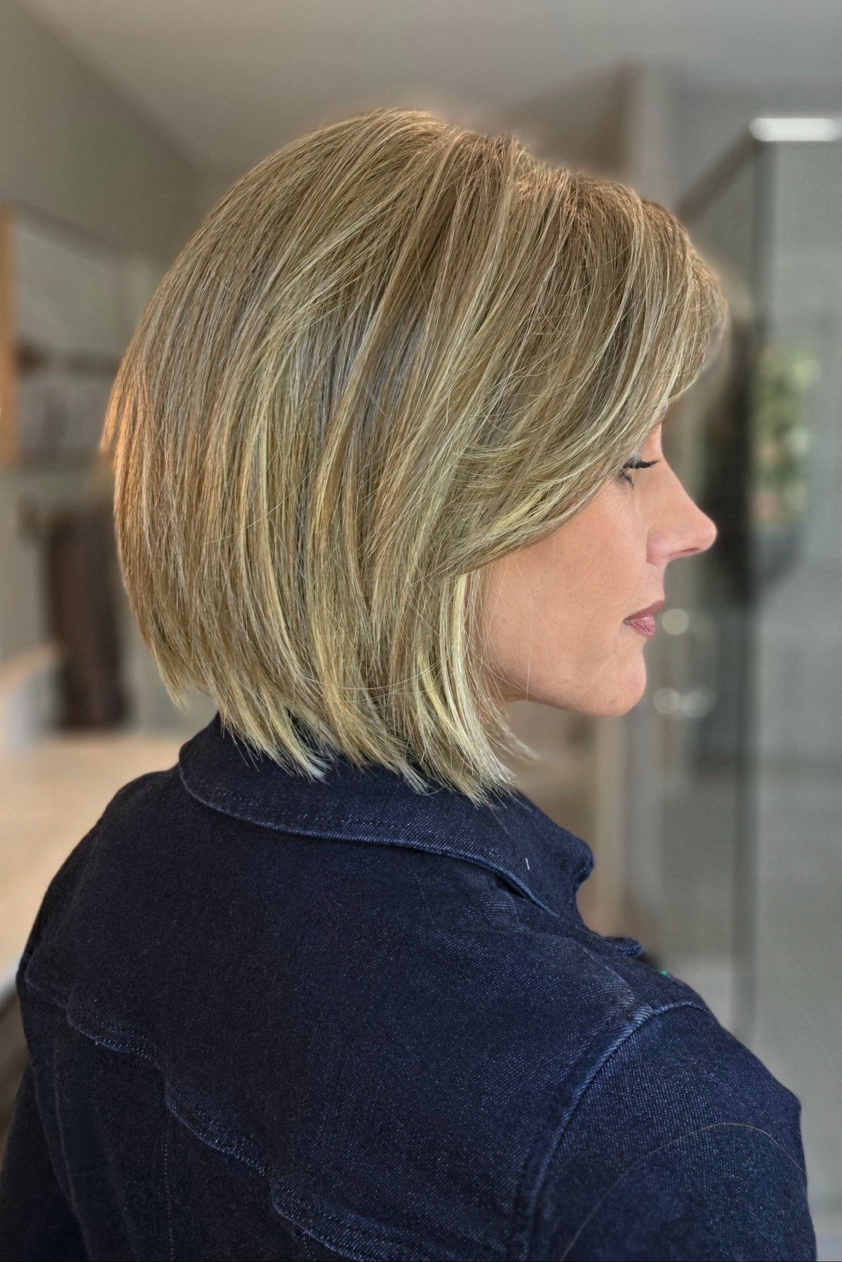 A smiling woman wearing a blonde bob wig with side bangs (Lark by Estetica in color R12/26CH). 