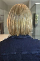 A smiling woman wearing a blonde bob wig with side bangs (Lark by Estetica in color R12/26CH). 