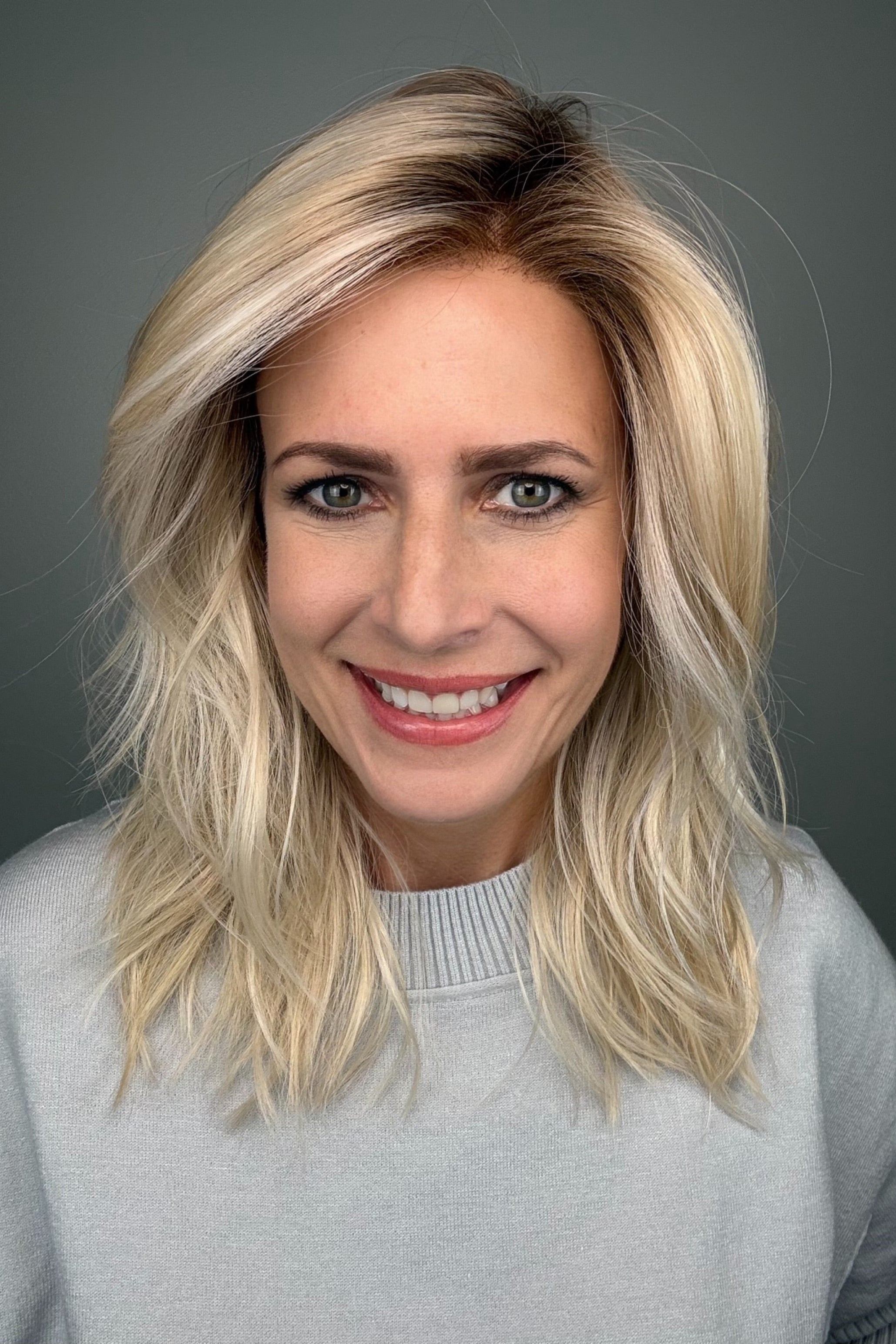 Woman wearing long layered wavy rooted blonde wig (Fenix by Estetica in Sunlit Blonde)