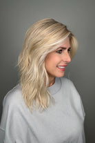 Woman wearing long layered wavy rooted blonde wig (Fenix by Estetica in Sunlit Blonde)
