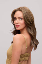Fiona Lite heat-friendly synthetic wig with long, flowing brown waves and a natural lace front hairline.