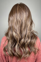 A smiling woman with long, wavy brown wig with blonde highlights (Fiona Lite by Jon Renau in color Mousse Cake).