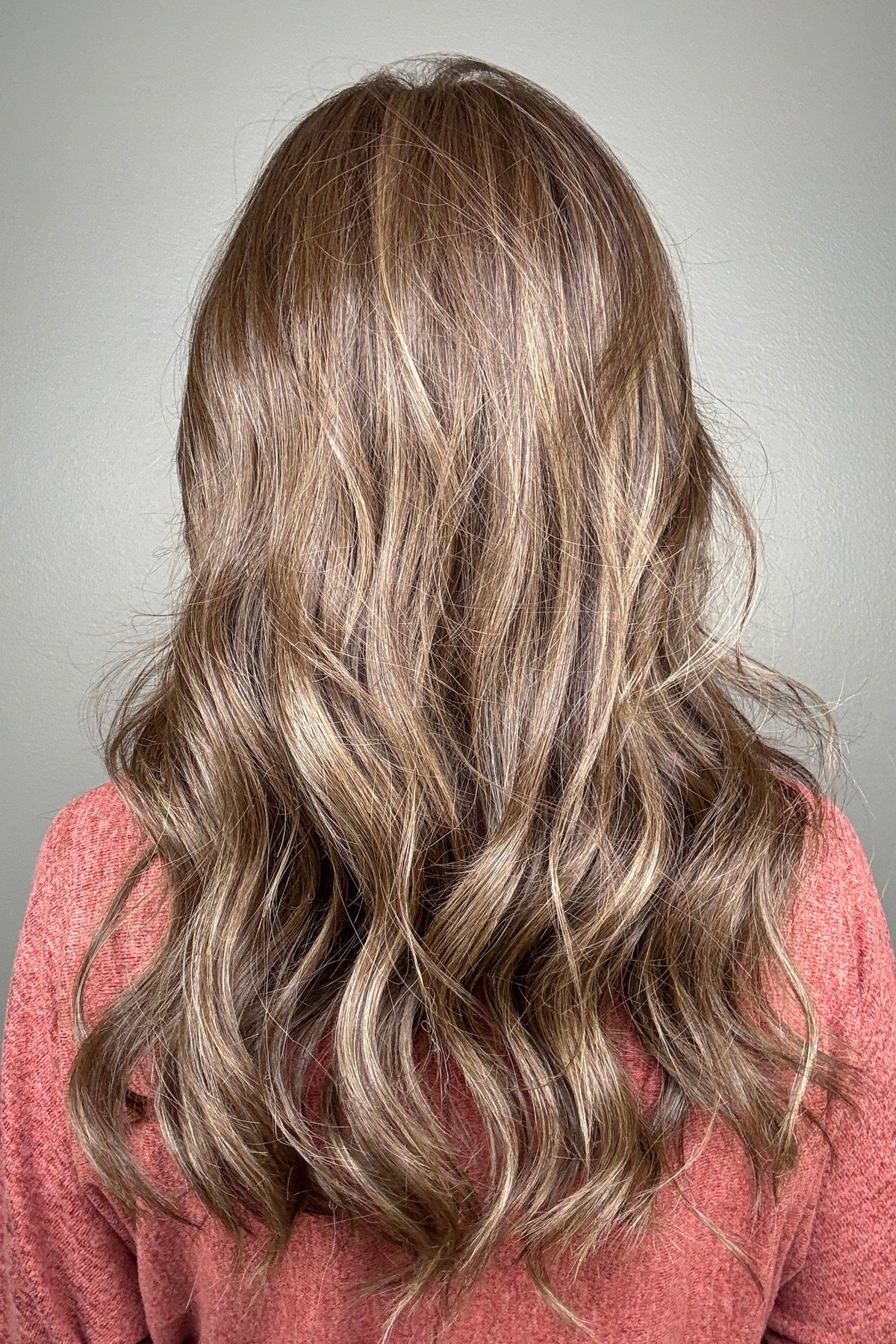 A smiling woman with long, wavy brown wig with blonde highlights (Fiona Lite by Jon Renau in color Mousse Cake).
