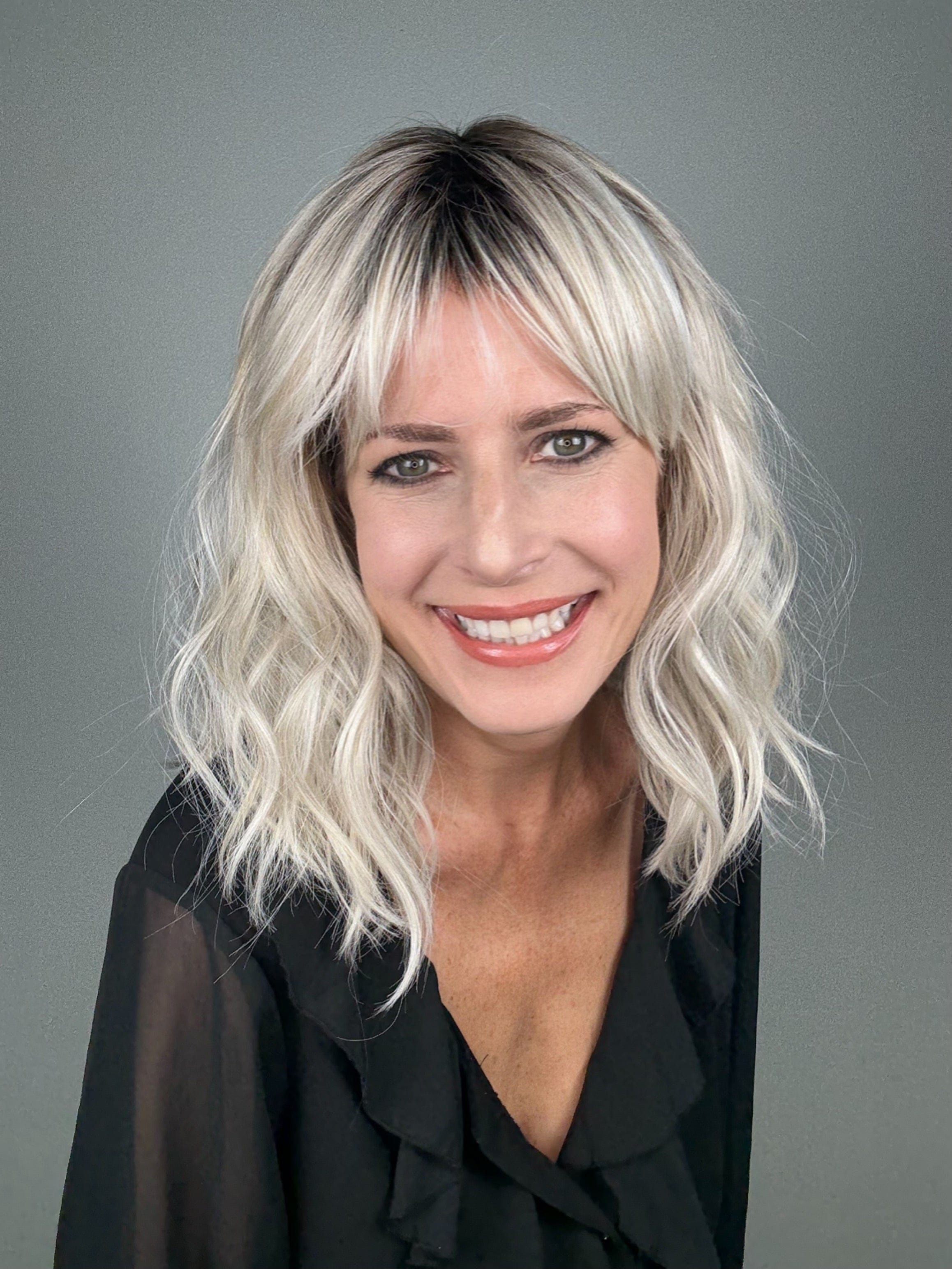 Woman wearing wavy rooted blonde wig with bangs (Frankie by Estetica in Silver Sun RT8)