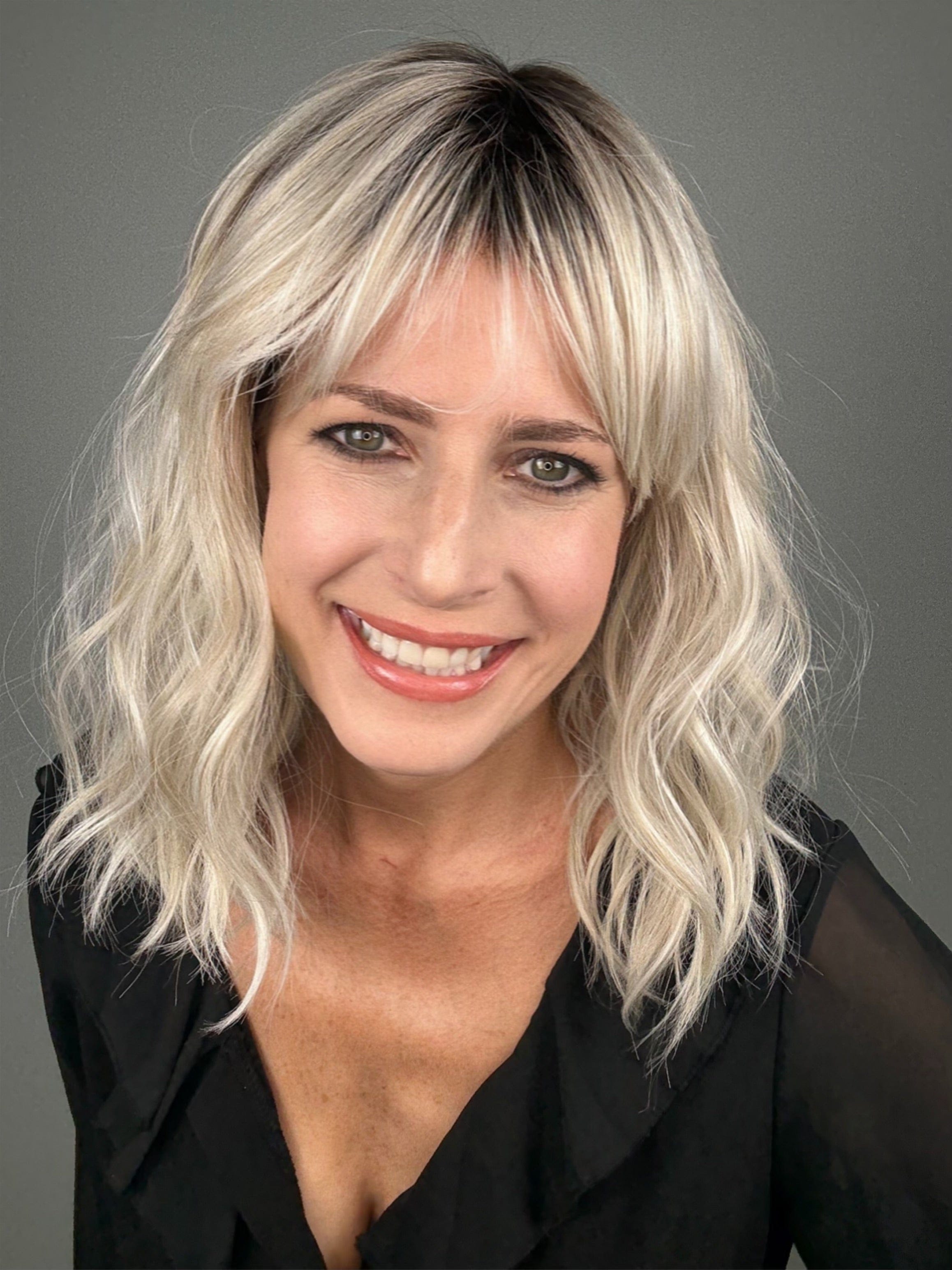 Woman wearing wavy rooted blonde wig with bangs (Frankie by Estetica in Silver Sun RT8)