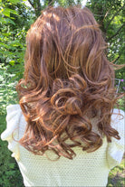 A woman wearing a shoulder-length red wig with highlighted streaks (Bouncing Belle by Gabor in Medium Red).