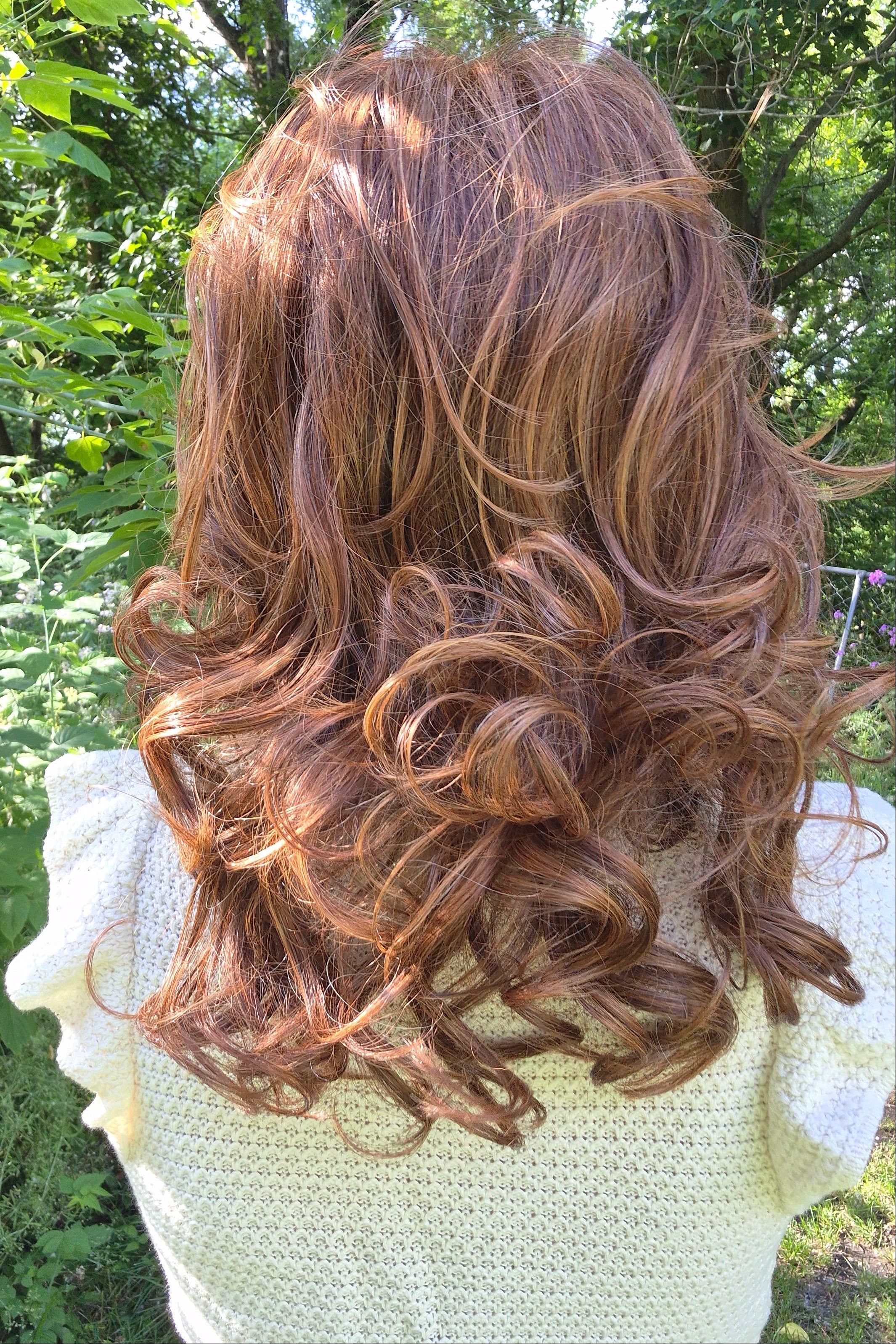 A woman wearing a shoulder-length red wig with highlighted streaks (Bouncing Belle by Gabor in Medium Red).