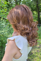A woman wearing a shoulder-length red wig with highlighted streaks (Bouncing Belle by Gabor in Medium Red).