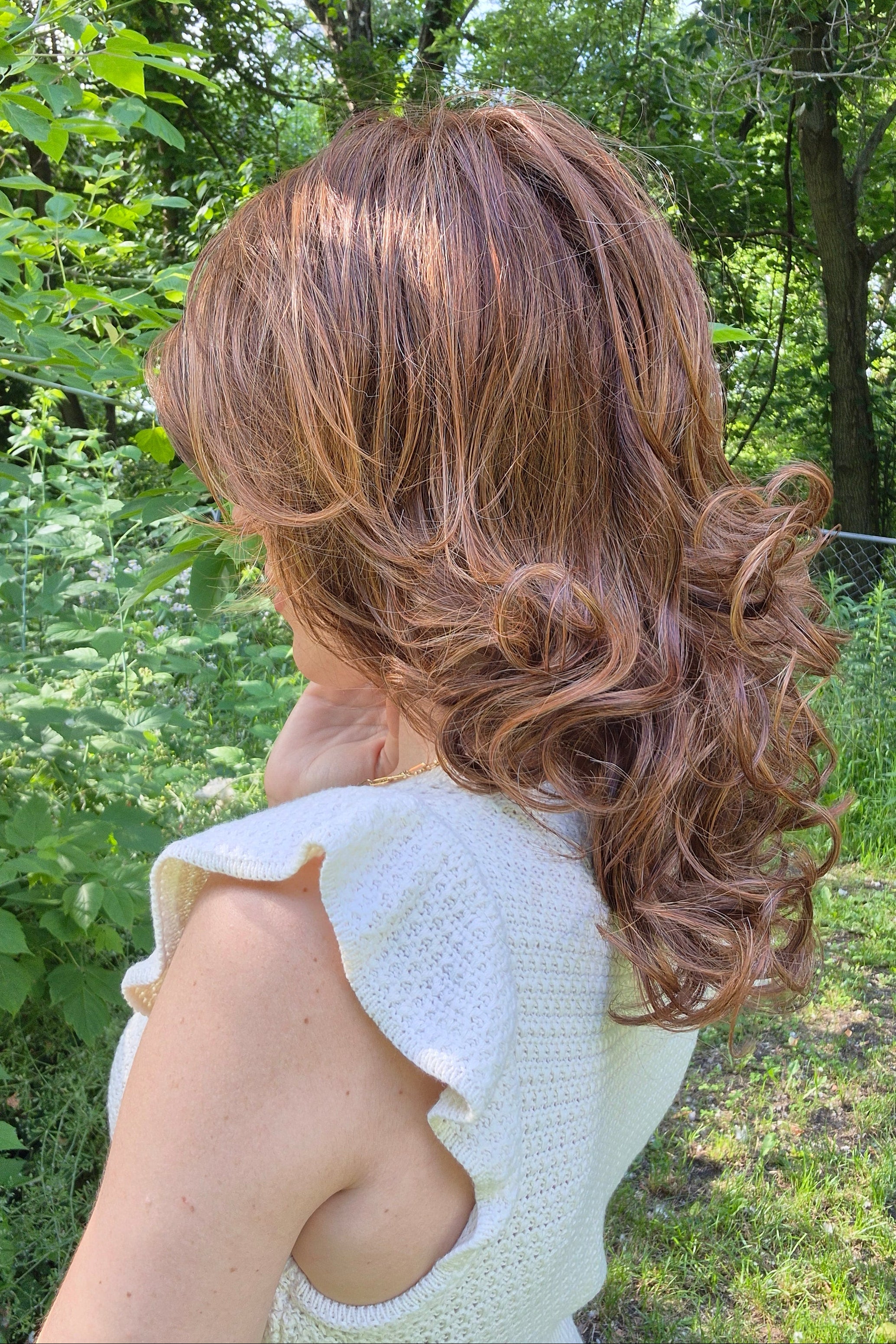 A woman wearing a shoulder-length red wig with highlighted streaks (Bouncing Belle by Gabor in Medium Red).