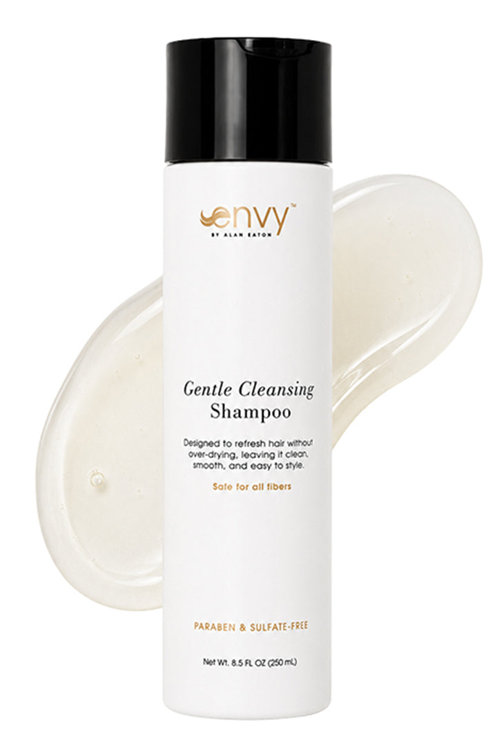 A bottle of Envy by Hair Gentle Cleansing Shampoo with a black cap and white bottle, shown in front of a translucent smear of the shampoo on a white background.
