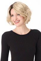Woman wearing a chin-length, textured blonde bob synthetic wig with soft layers and a dark root.