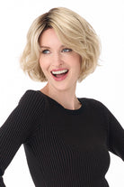 Gia by Envy chin-length textured blonde bob wig with soft layers and dark roots on a smiling woman.