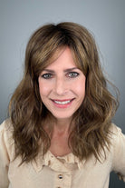 A woman with shoulder-length brown hair and bangs, wearing a light beige ruffled blouse (Great Vibe by Toni Brattin in color Brown Blonde).