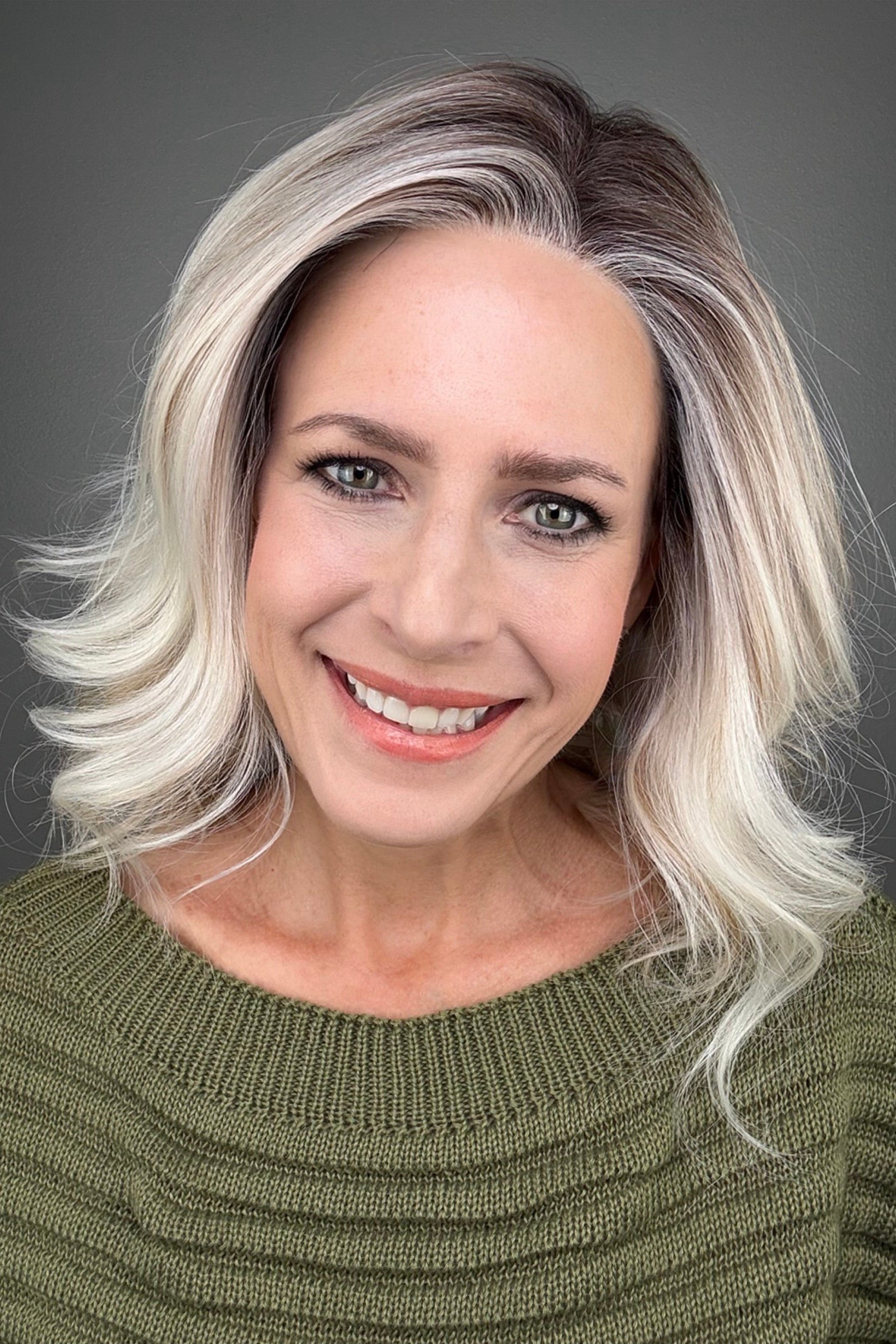 A smiling woman with shoulder-length highlighted wig in shades of platinum blonde and brown (Indie by PUSH Hair in color Pearl Silk R).