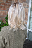 A woman with shoulder-length layered blonde hair wearing an olive green cable-knit sweater (Sloane by Jon Renau in Catalina Blonde).
