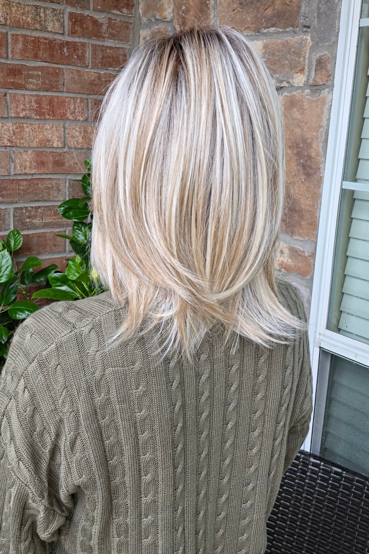 A woman with shoulder-length layered blonde hair wearing an olive green cable-knit sweater (Sloane by Jon Renau in Catalina Blonde).