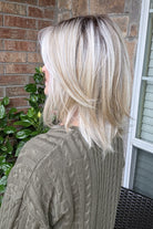 A woman with shoulder-length layered blonde hair wearing an olive green cable-knit sweater (Sloane by Jon Renau in Catalina Blonde).