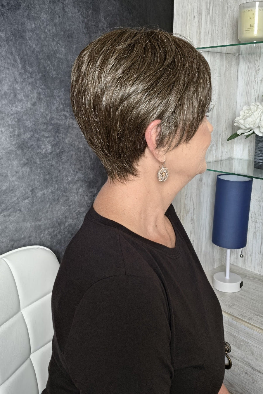 A woman with a short, layered brown and blonde bob hairstyle wearing a black long-sleeve top (Tess by Jon Renau in color Milkshake).