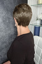 A woman with a short, layered brown and blonde bob hairstyle wearing a black long-sleeve top (Tess by Jon Renau in color Milkshake).
