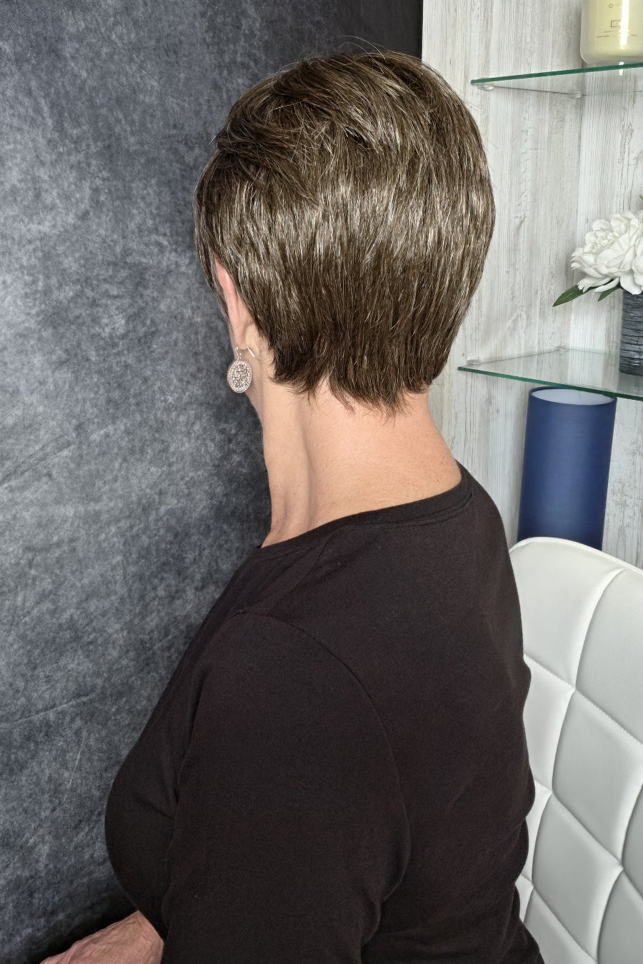 A woman with a short, layered brown and blonde bob hairstyle wearing a black long-sleeve top (Tess by Jon Renau in color Milkshake).