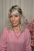 A woman with shoulder-length wavy pink-blonde wig with bangs styled (Frankie by Estetica in color Polarizing Pink).