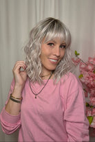 A woman with shoulder-length wavy pink-blonde wig with bangs (Frankie by Estetica in color Polarizing Pink).
