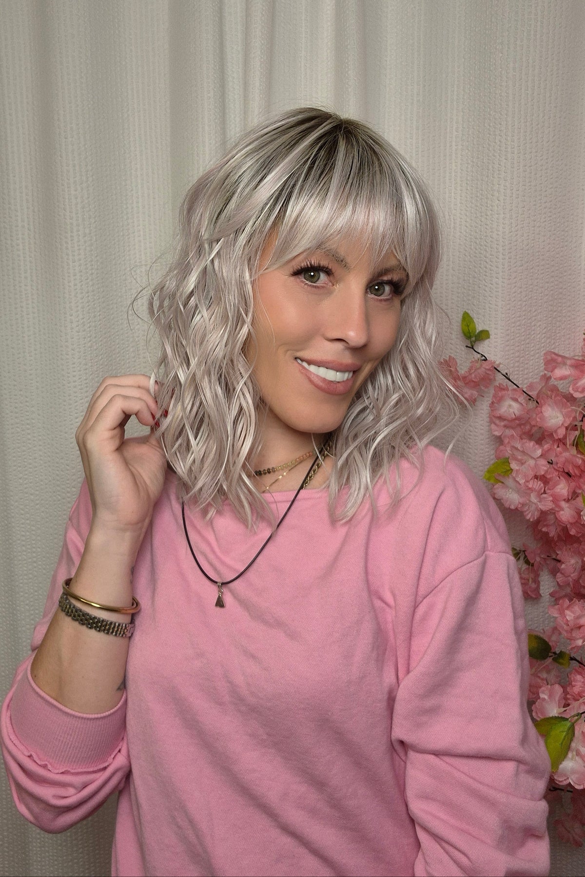 A woman with shoulder-length wavy pink-blonde wig with bangs (Frankie by Estetica in color Polarizing Pink).
