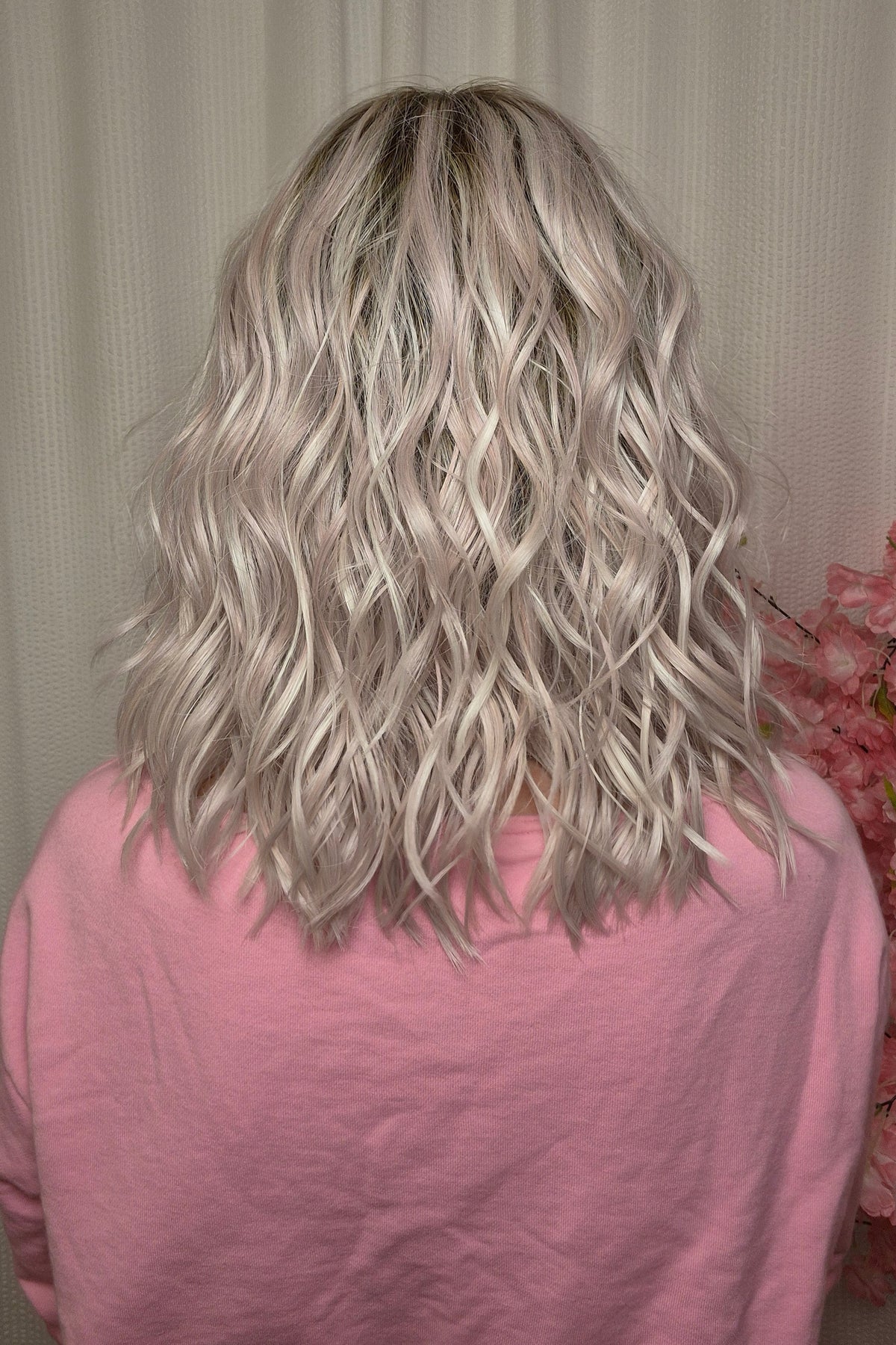 A woman with shoulder-length wavy pink-blonde wig with bangs (Frankie by Estetica in color Polarizing Pink).
