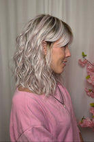 A woman with shoulder-length wavy pink-blonde wig with bangs (Frankie by Estetica in color Polarizing Pink).