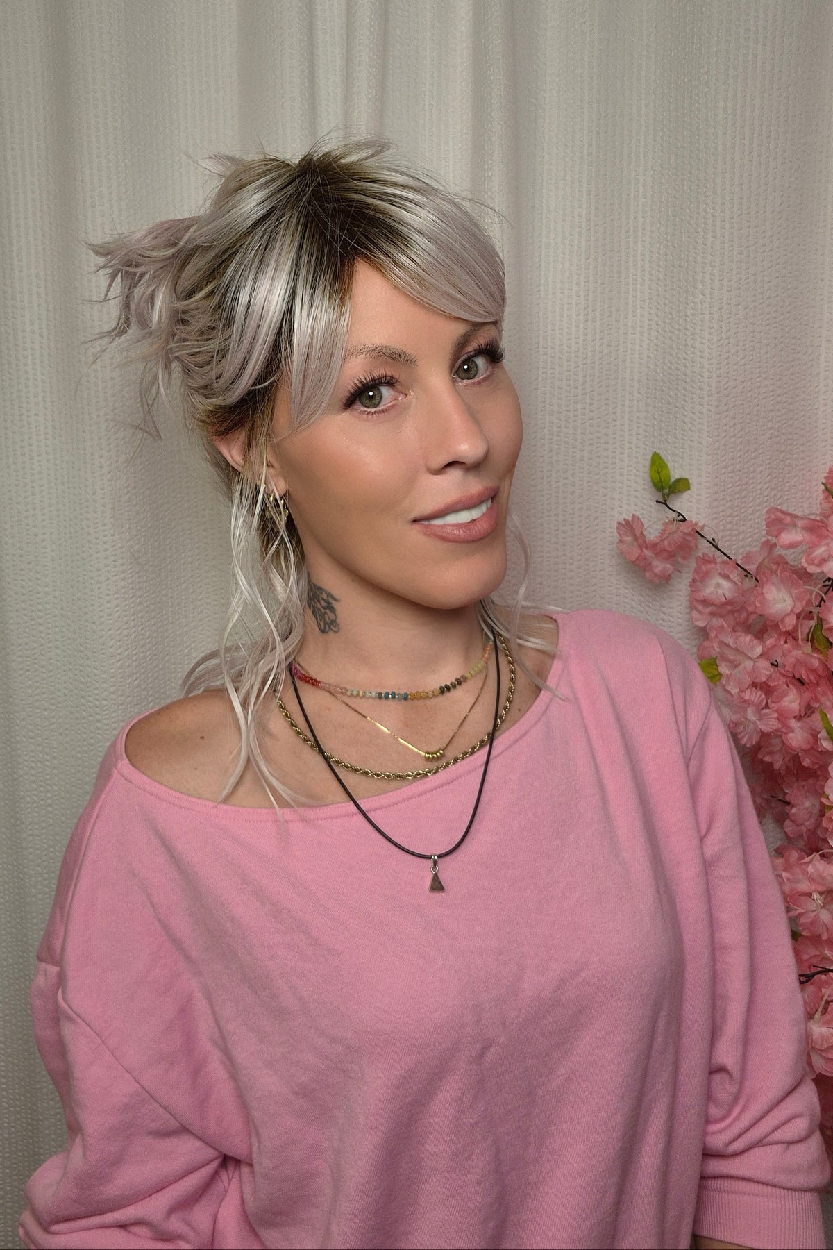 A woman with shoulder-length wavy pink-blonde wig with bangs styled (Frankie by Estetica in color Polarizing Pink).