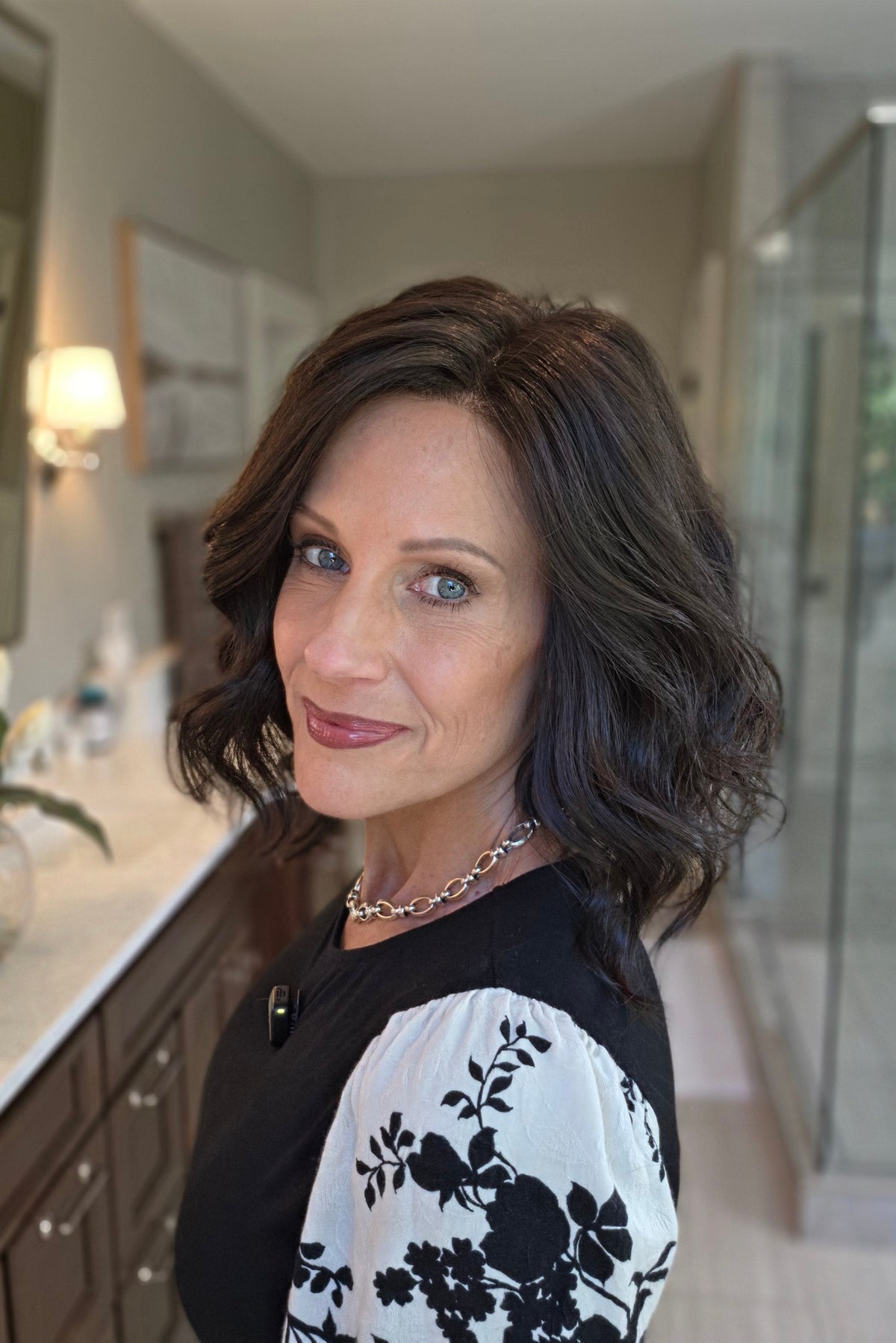 A smiling woman with shoulder-length dark brown wavy wig (Lacy Lite by Jon Renau in 4).