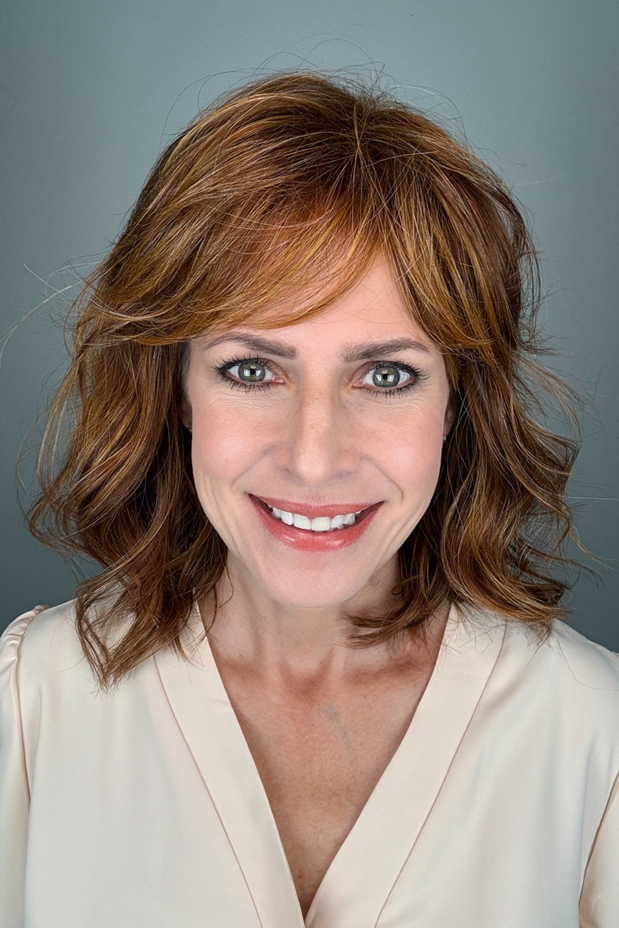 A woman with a shoulder-length wavy red wig with bangs (Lively by Gabor in Medium Red).