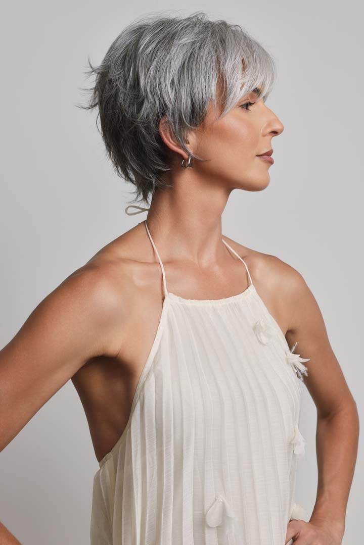 Mio by Noriko short grey layered pixie wig with a lace front and monofilament part on a woman in a white dress.