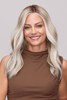 Woman wearing Morgan by Jon Renau, long, wavy platinum blonde hair wearing a brown mock-neck top, photographed against a solid light gray background.