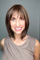 A smiling woman with a shoulder-length brown bob haircut and straight bangs (Ami by Noriko in color Marble Brown-R)