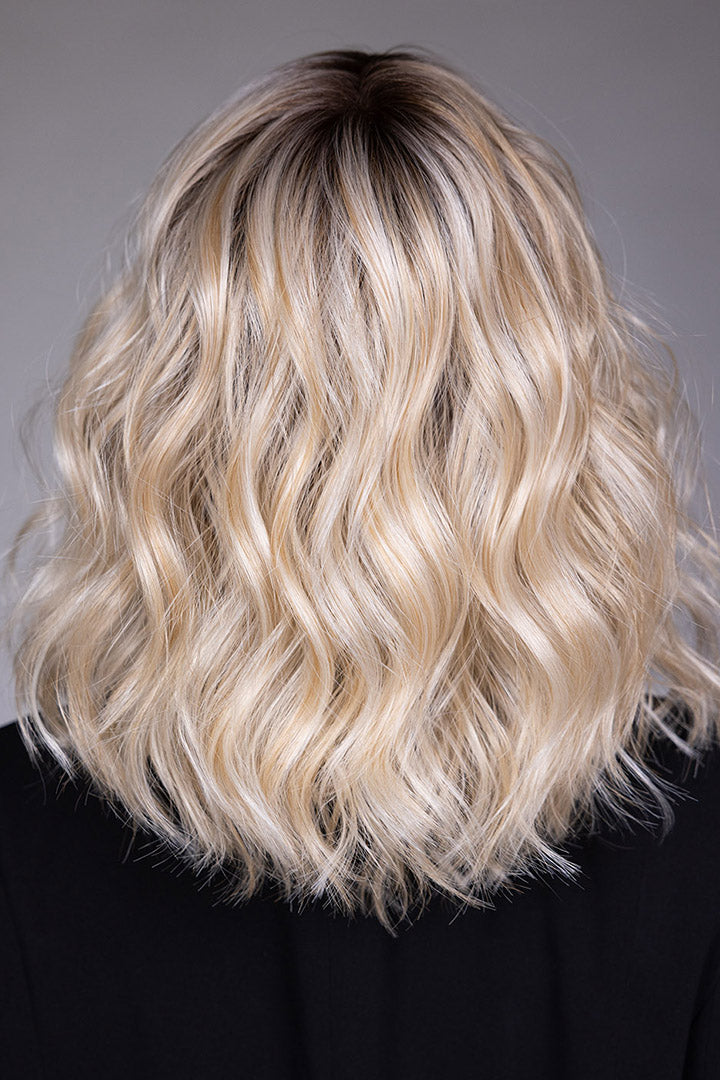Back view of a shoulder-length blonde wavy bob wig with dark roots and textured layers by Belle Tress.