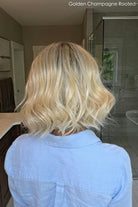 Woman wearing shoulder length curly blonde wig (Brielle by PUSH Hair in color Golden Champagne R)