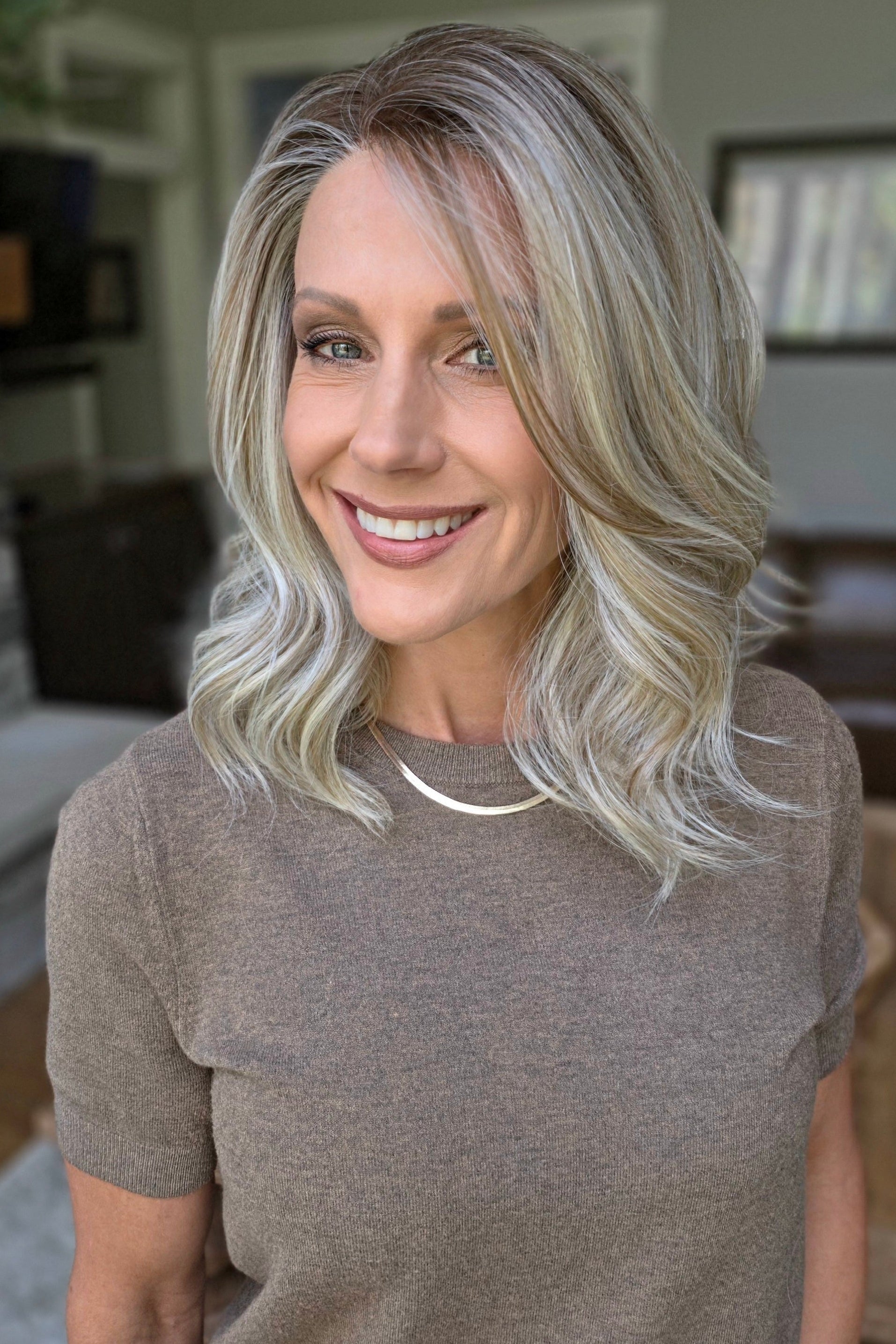 A smiling woman with shoulder-length wavy blonde wig (Keeley by PUSH Hair in color Champagne Blonde R).