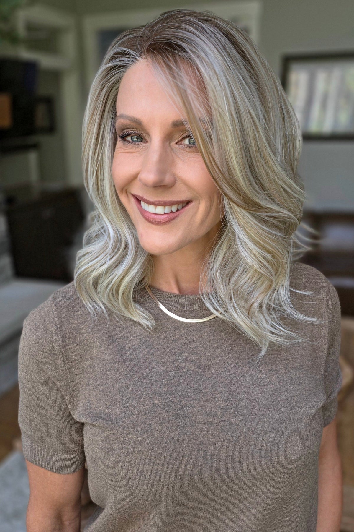 A smiling woman with shoulder-length wavy blonde wig (Keeley by PUSH Hair in color Champagne Blonde R).
