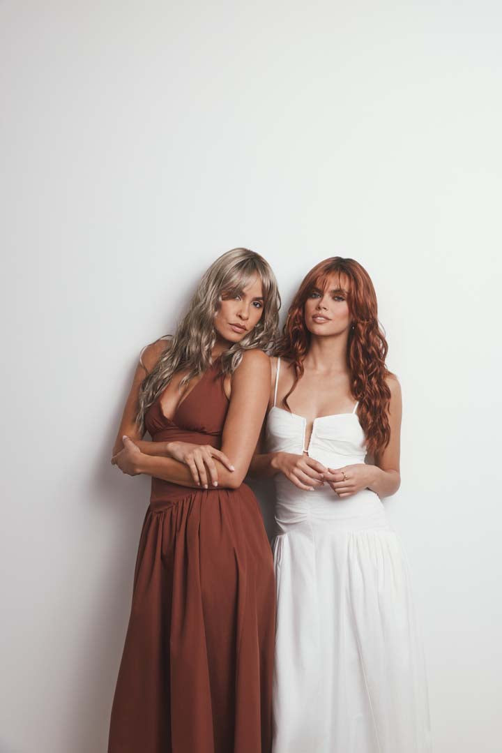 Two women wearing long, wavy Phillipa synthetic lace front wigs in blonde and auburn shades with face-framing fringe.