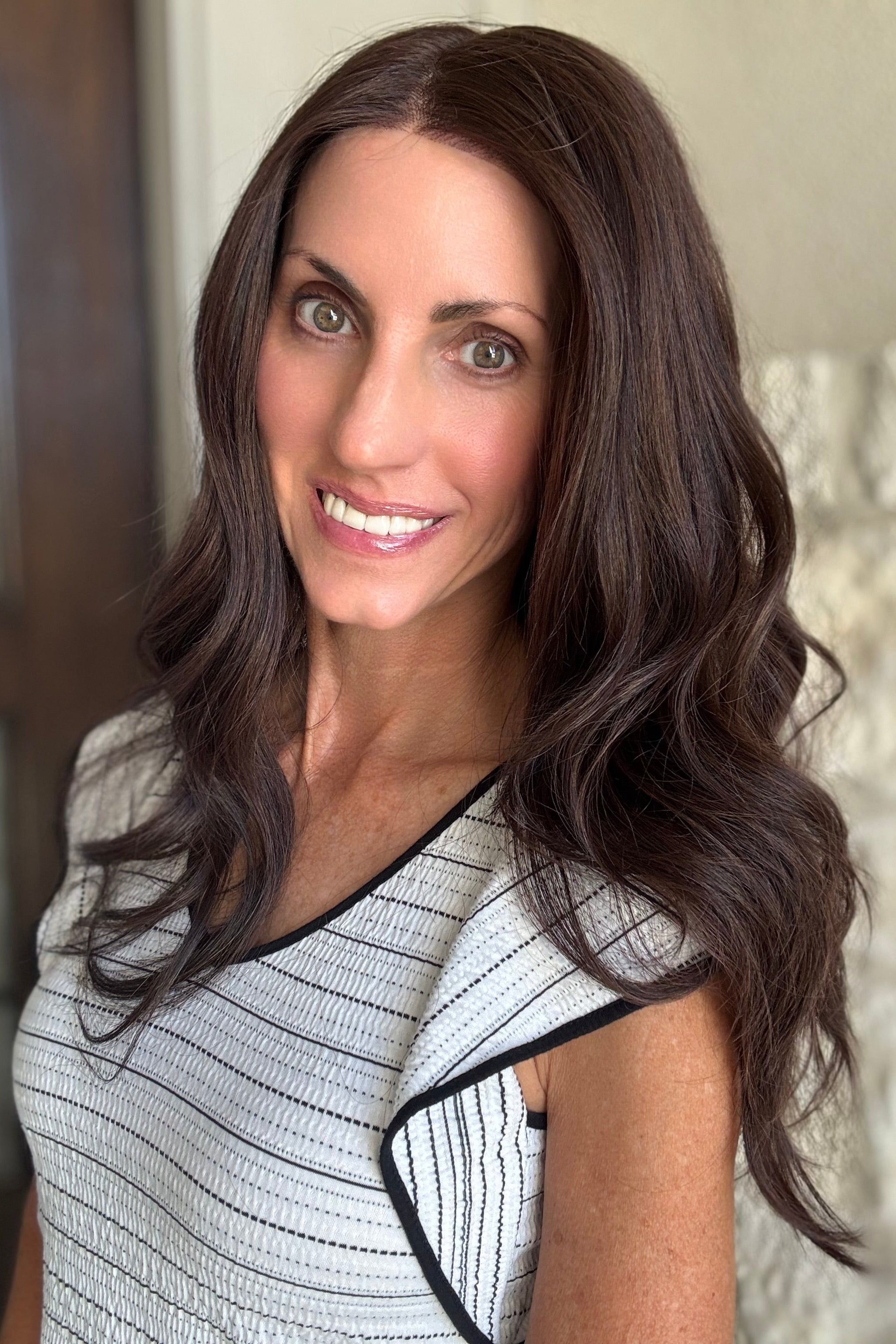 A woman with long, wavy dark brown hair wearing a black and white striped sleeveless top with black trim (Bradley by PUSH Hair in color Dark Chocolate Chestnut). 