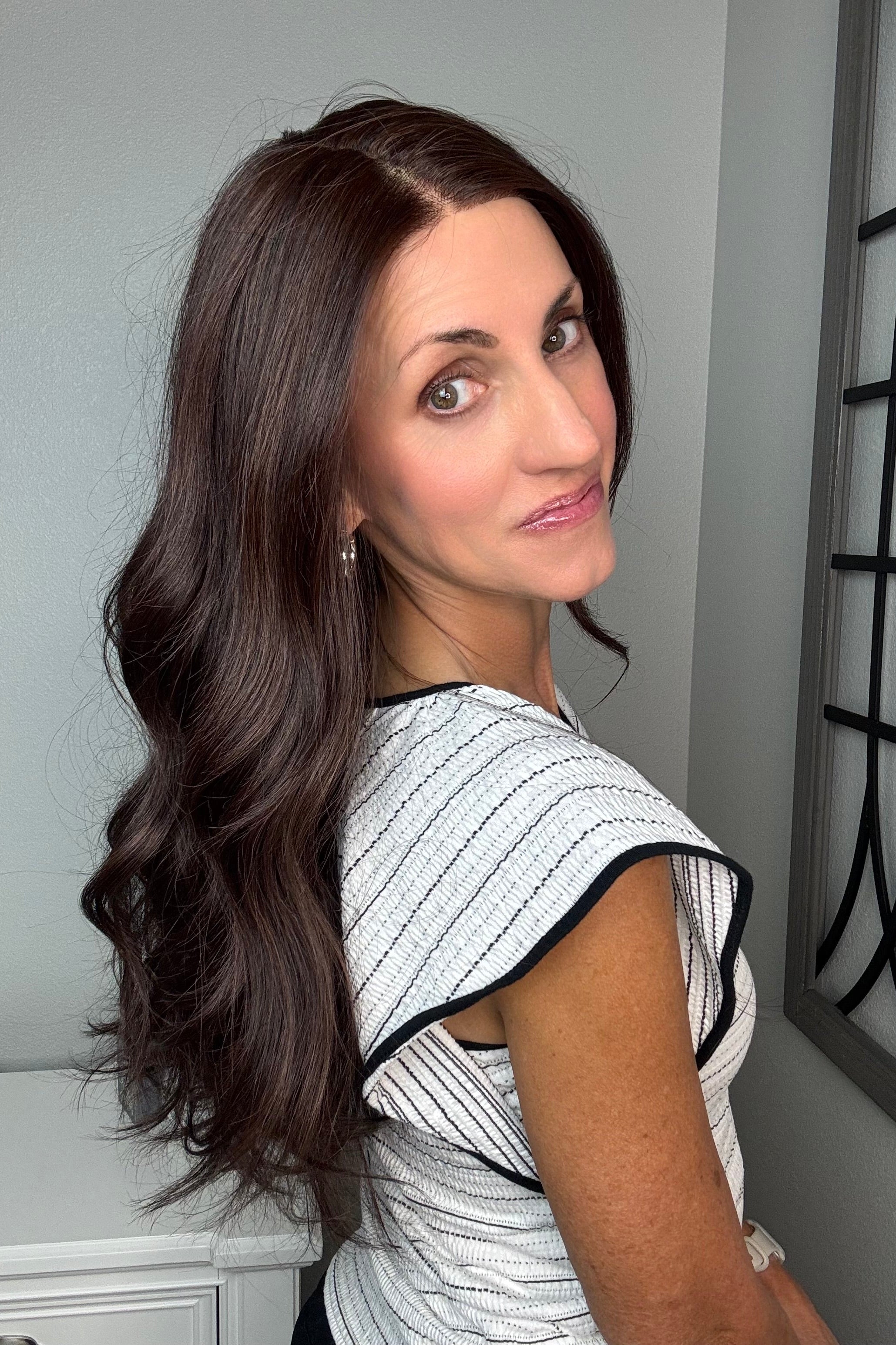 A woman with long, wavy dark brown hair wearing a black and white striped sleeveless top with black trim (Bradley by PUSH Hair in color Dark Chocolate Chestnut). 