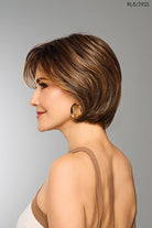 Woman with a brown Raquel Welch wig against a gray background